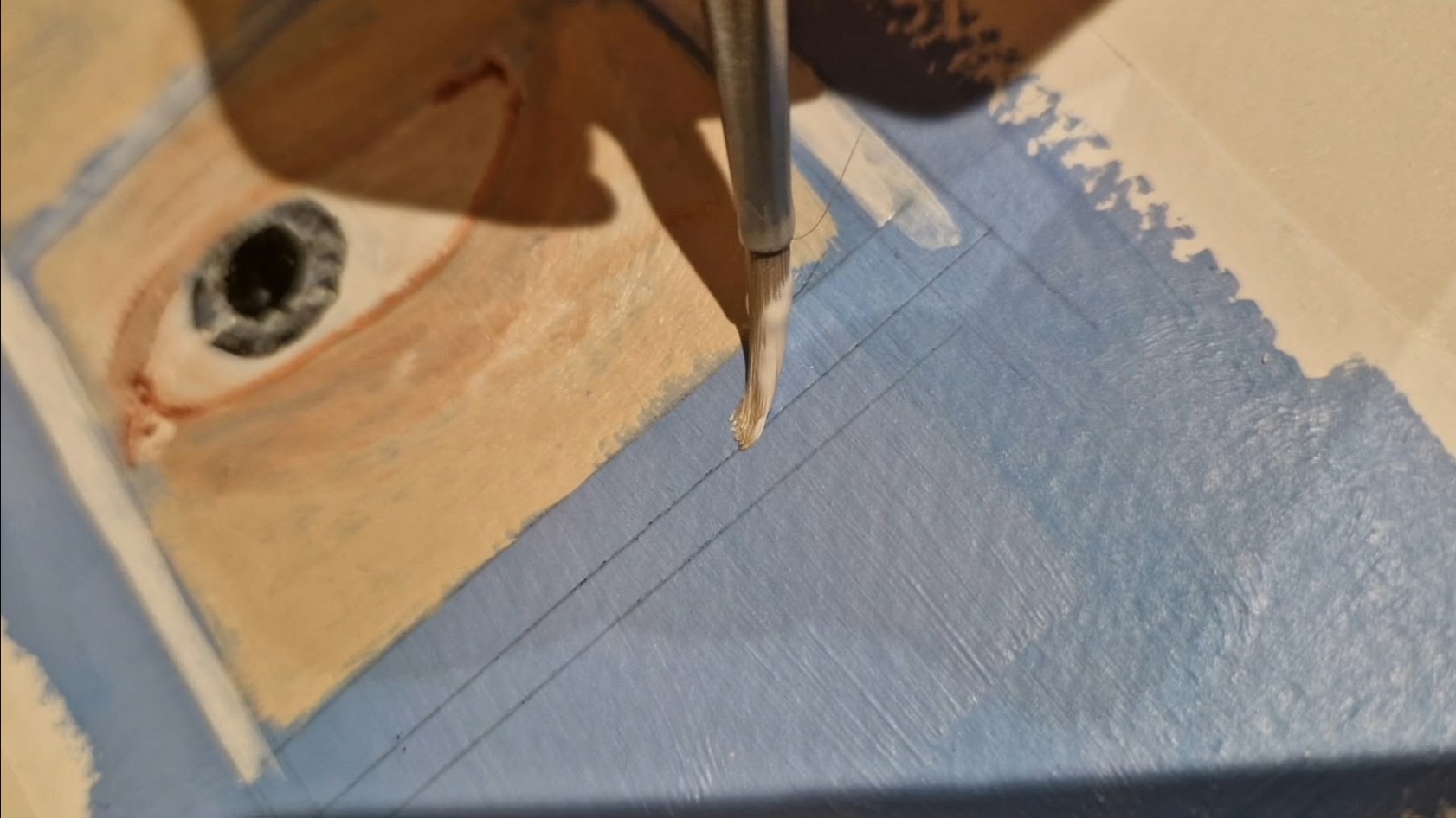 A paintbrush with white acrylic being applied to a blue background. Close Up.